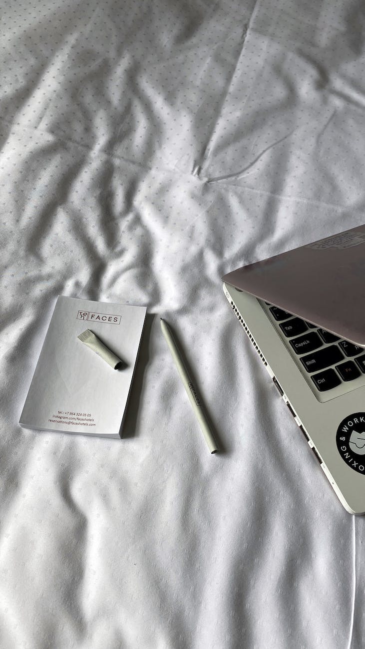 laptop pencil and book on bedclothes